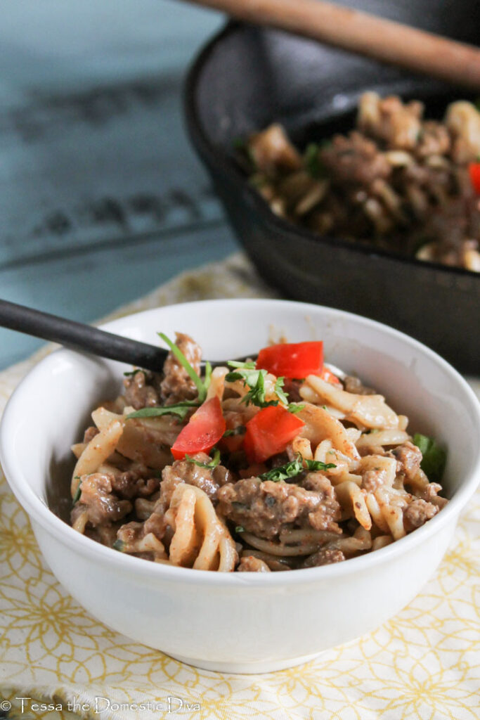 a white filled with noodles, ground beef in a savory cheesy sauce with a red pepper garnish