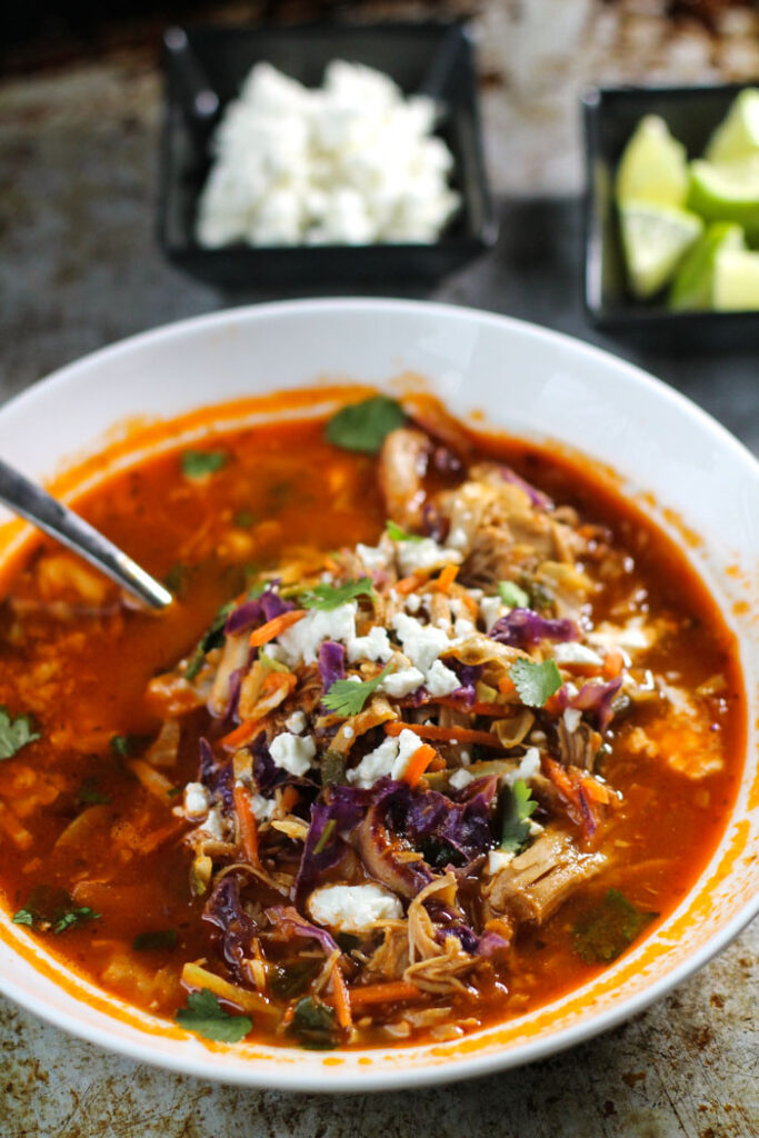 white bowl of a rich tomato broth with chicken, cabbage, and white crumbled cheese