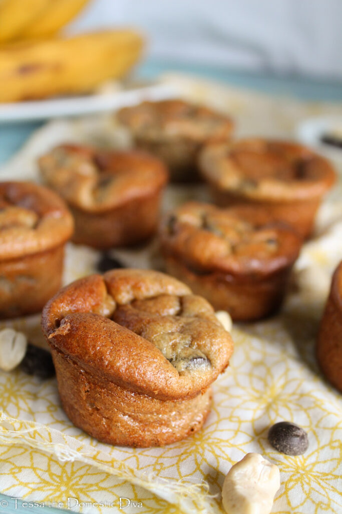 several chocolate chip studded mini muffins arranged on a pale yellow cloth with a raw cashew and a rip banana in background