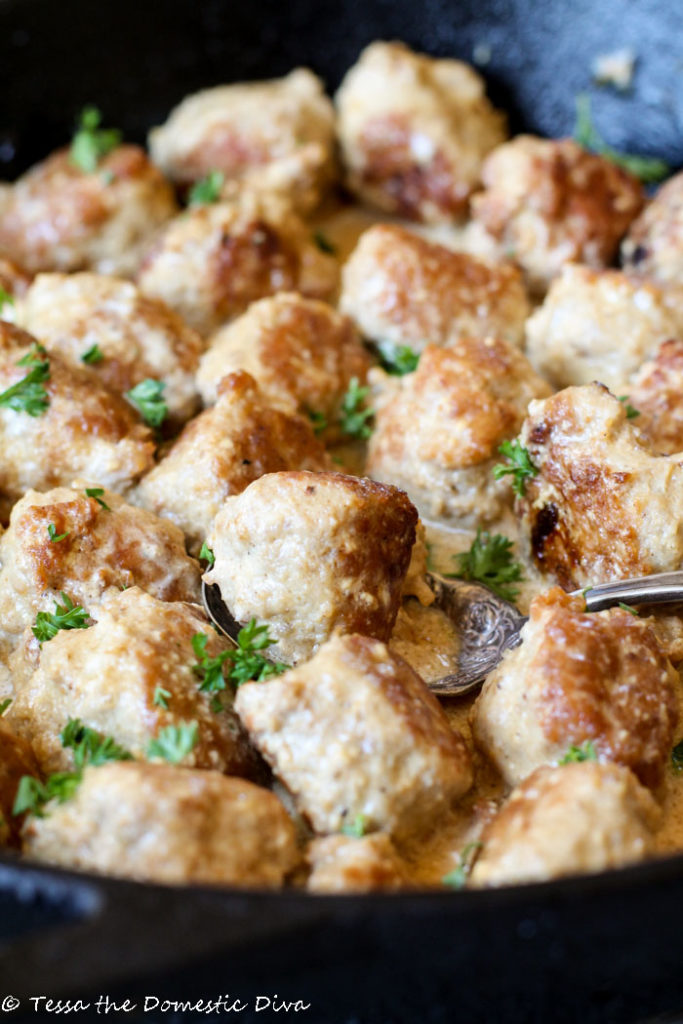 browned turkey meatballs in a creamy sauce nestled in a cast iron skillet and a fresh parsley garnish