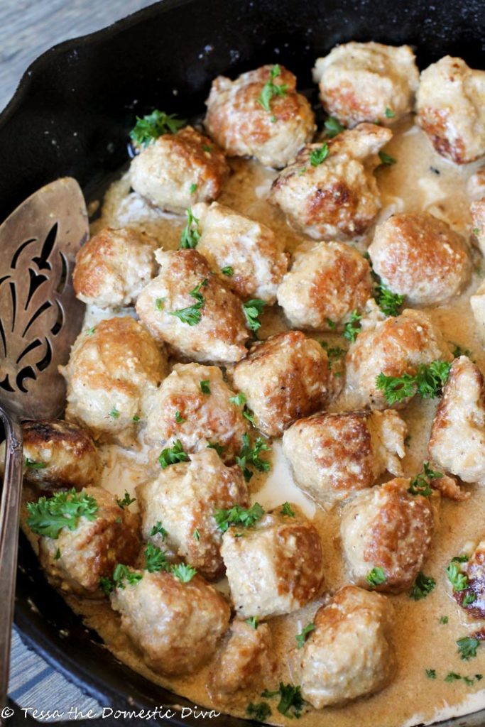browned poultry meatballs in a creamy sauce with fresh parsley in cast iron pan