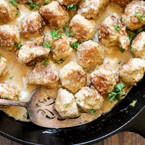 birdseye view of a black cast iron skillet filled with golden turkey meatballs in a creamy sauce with a fresh parsley garnish