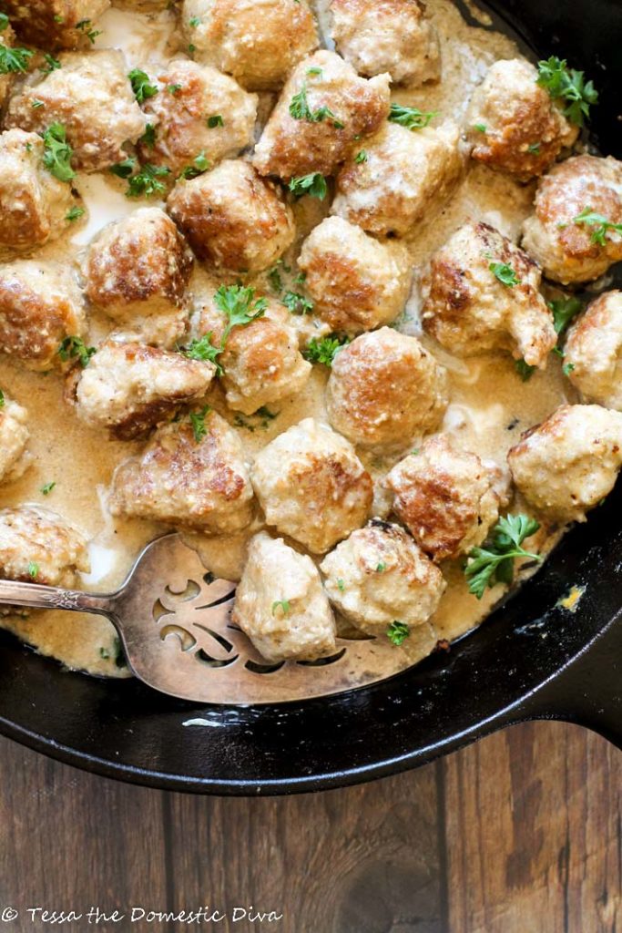 birdseye view of a black cast iron skillet filled with golden turkey meatballs in a creamy sauce with a fresh parsley garnish