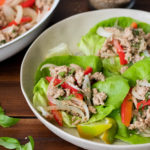 frontal view of two white bowls atop a dark wooden surface filled with butter lettuce leaves topped with ground turkey and red bell peppers and fresh basil