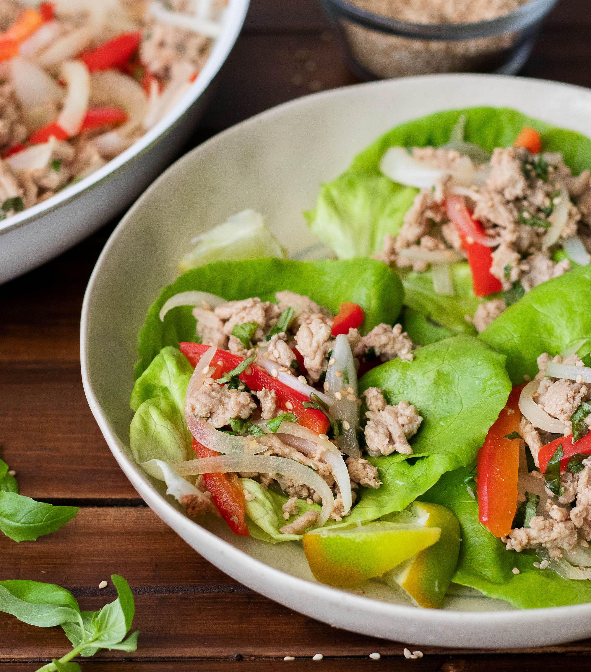 frontal view of two white bowls atop a dark wooden surface filled with butter lettuce leaves topped with ground turkey and red bell peppers and fresh basil