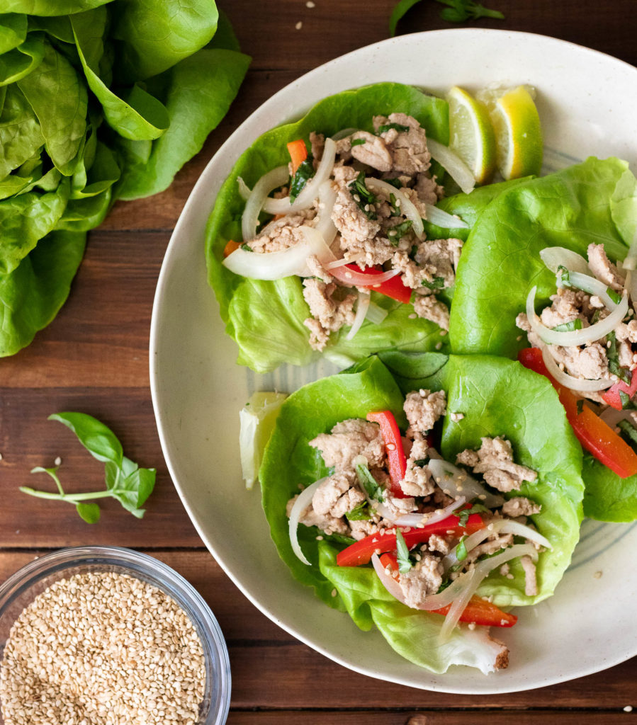 birdseye view of a white bowl with three butter lettuc leaves filled with ground turkey, red bell peppers, and sesame seeds