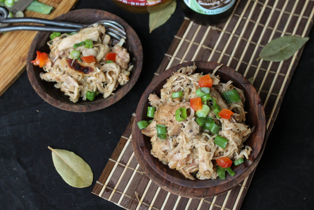 birds eye view of two wooden bowls filled with tender shredded chicken adobo with green onions and red pepper garnish