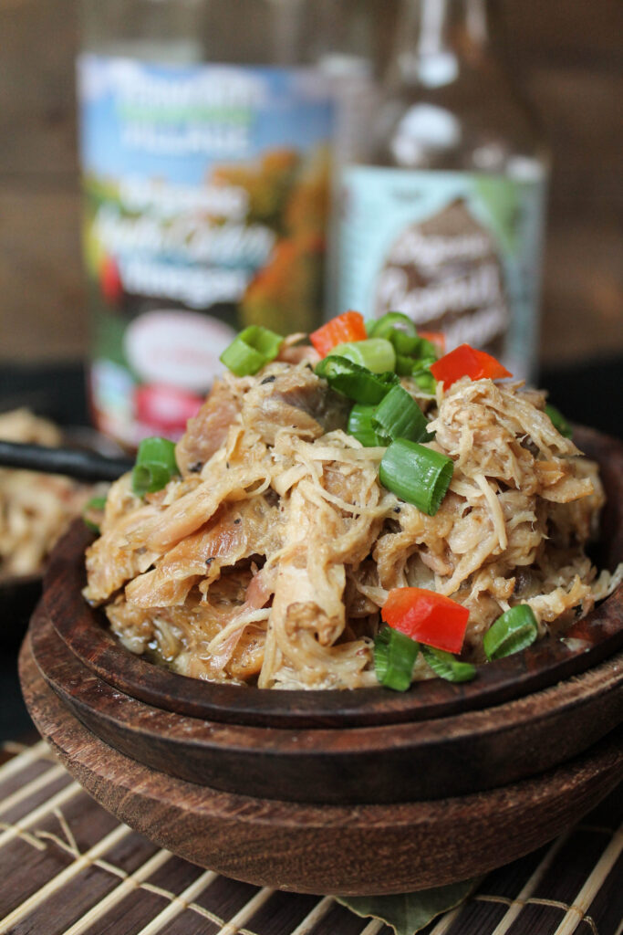 close up front view of several stacked wooden bowls with tender shredded chicken thighs with scallions and red peppers