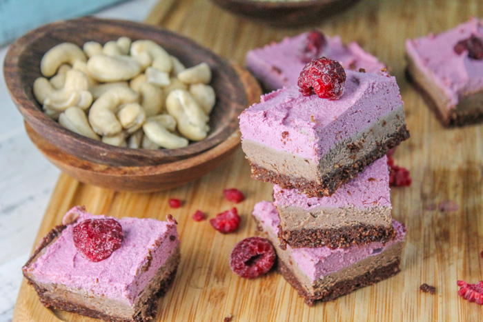 several square of a dairy free raspberry cheesecake bars with chocolate and fresh berries