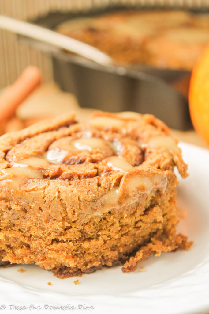 a single pumpkin cinnamon roll on a white plate with a pan in the background