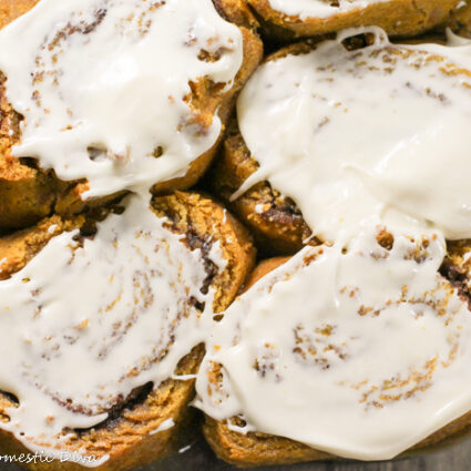 overhead shot of a glass rectangle baking pan fill with cream cheese frosted pumpkin cinnamon rolls