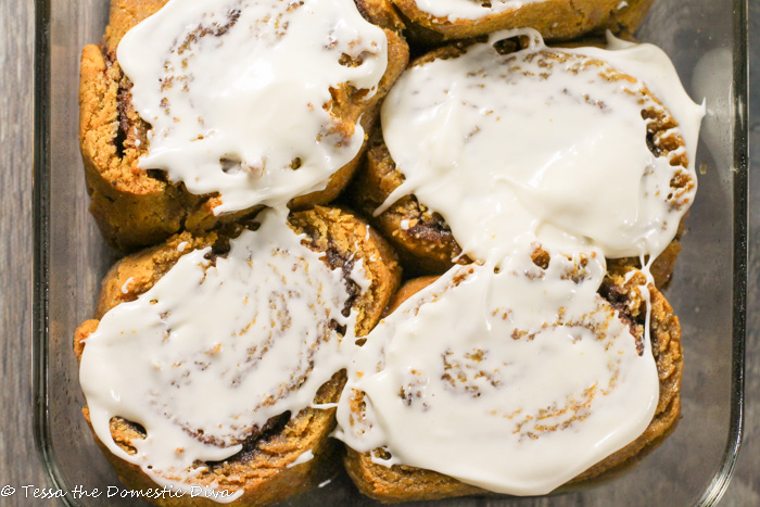 overhead shot of a glass rectangle baking pan fill with cream cheese frosted pumpkin cinnamon rolls