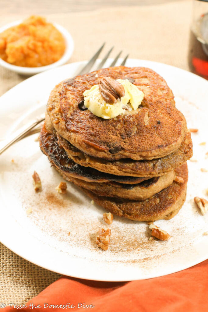 a white plate with orange tinted pancakes with pumpkin puree and cinnamon in background