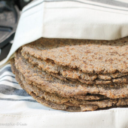 a stack of brown tinted wholegrain fresh tortillas wrapped in a white cloth with a cast iron tortilla press