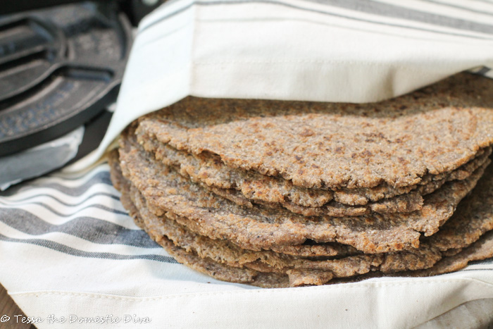 a stack of brown tinted wholegrain fresh tortillas wrapped in a white cloth with a cast iron tortilla press