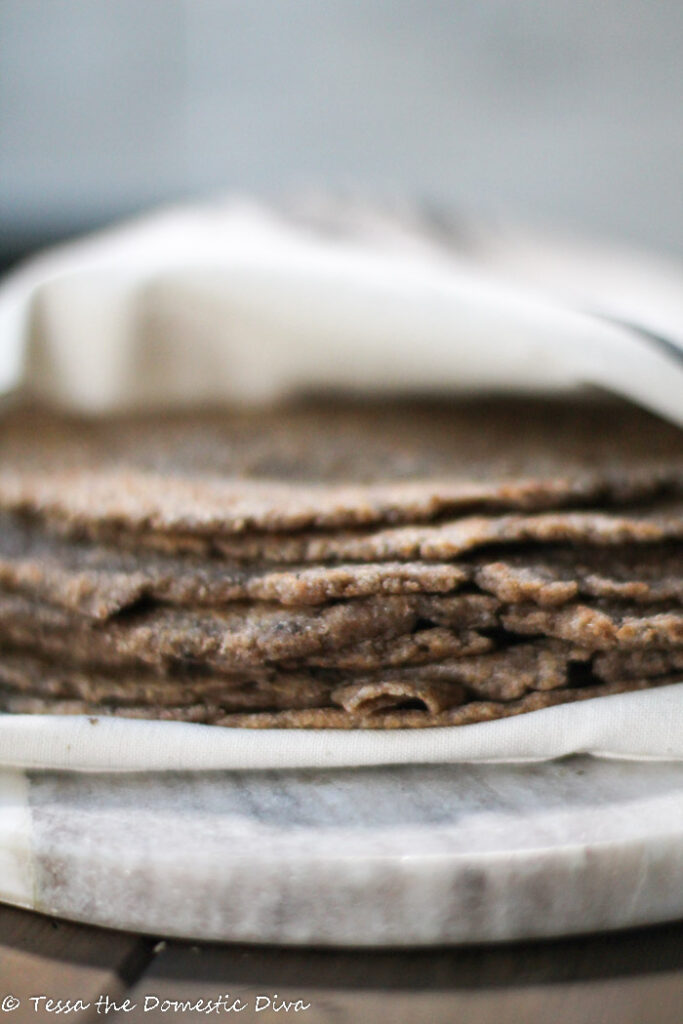 a stack of many wholegrain brown tortillas wrapped in a off white linen