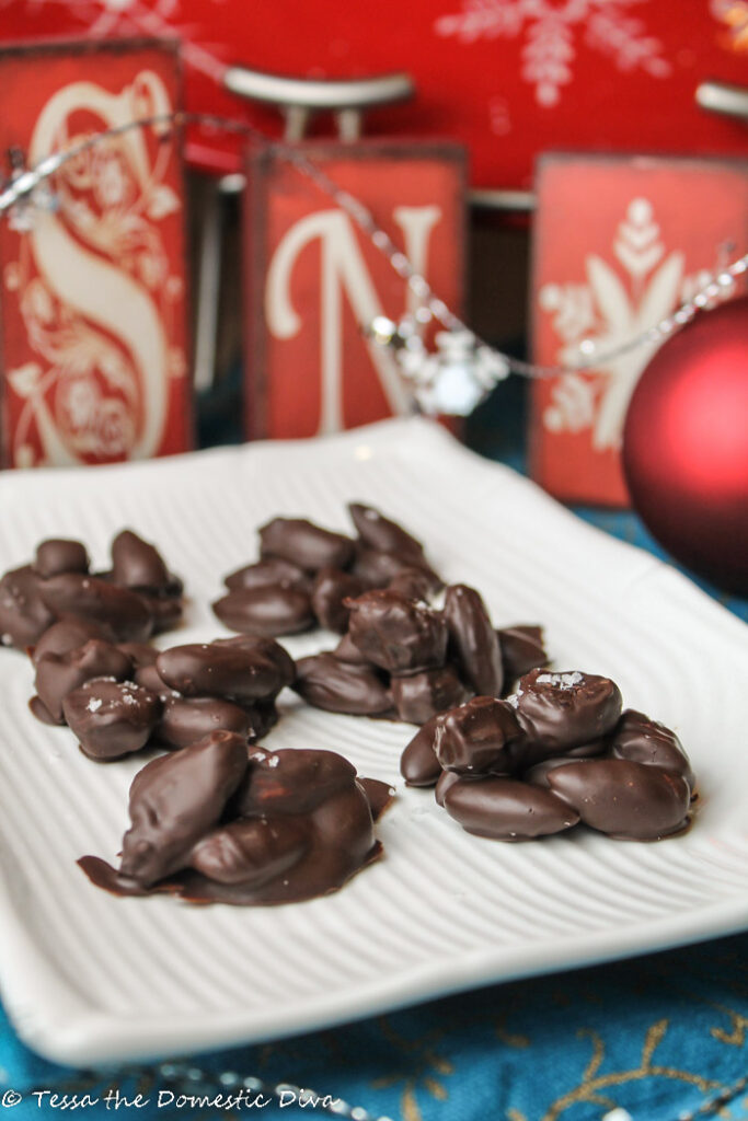  chocolate covered almonds and dried fruit on a white plate with holiday decor in the background
