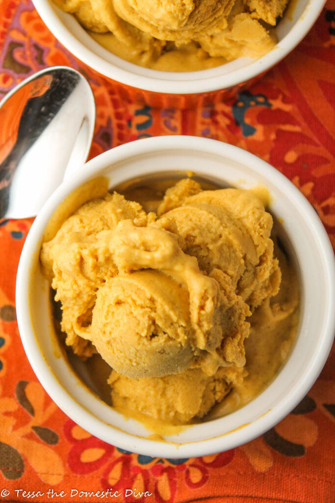 Birdseye view of two ramekins filled with a creamy orange pumpkin ice cream atop a orange floral fall themed cloth