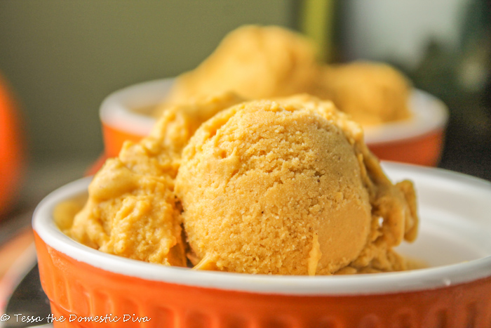 eye level close up of orange ramekin filled with scoops of creamy orange pumpkin ice cream on a wooden cutting board