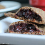 close up of a halved sweet empanada filled with berries and chocolate on a white plate