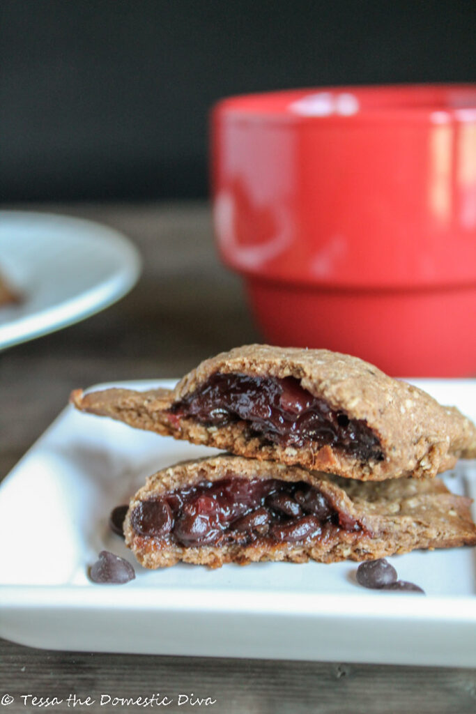 a white square plate with a halved berry and chocolate filled empanada