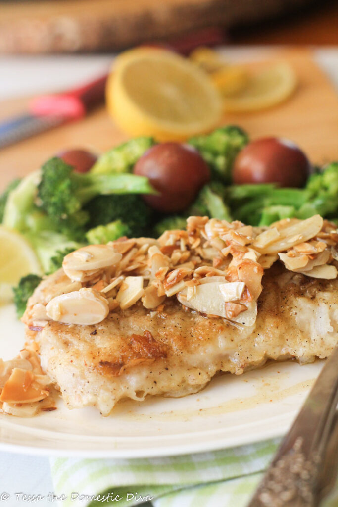 a piece of white fish crisped and topped with a butter, lemon, garlic, and almond sauce with fresh tomatoes and steamed broccoli