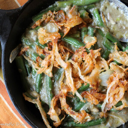 cast iron skillet filled with blancehd green beans in a creamy mushroomsauce and crispy onion topping