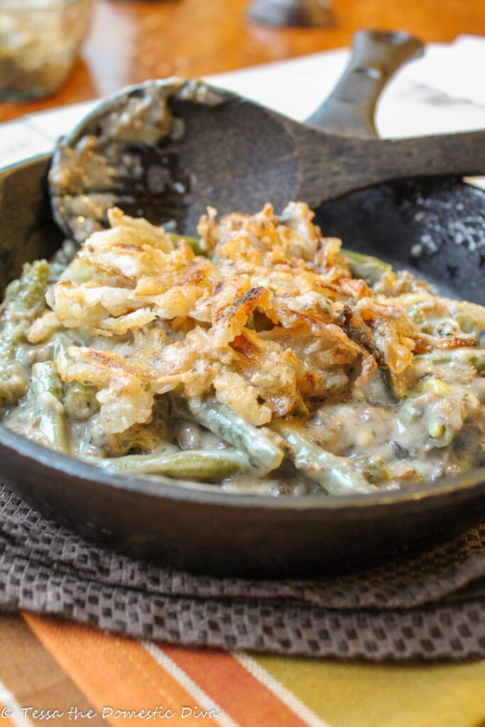 a black cast iron skillet filled with blanched green beans in a creamy mushroom sauce and topped with crispy fried onions