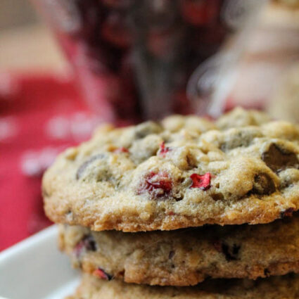three stacked oatmeal cookies on a square white plate with a cup of fresh cranberries in background