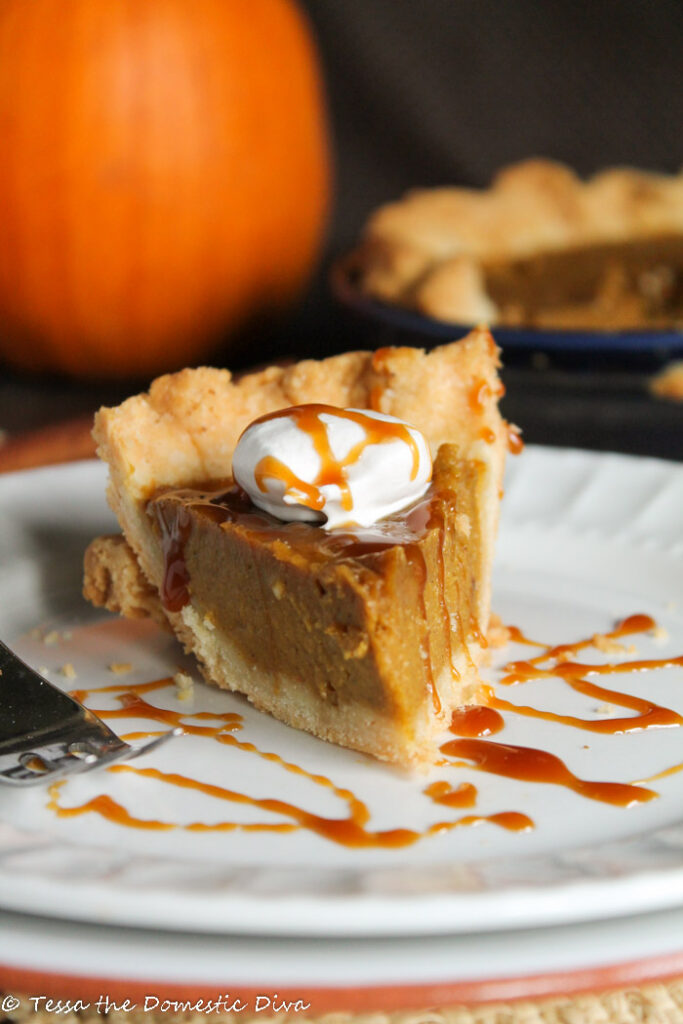 a slice of pumpkin pie of white plate with a drizzle of caramel sauce