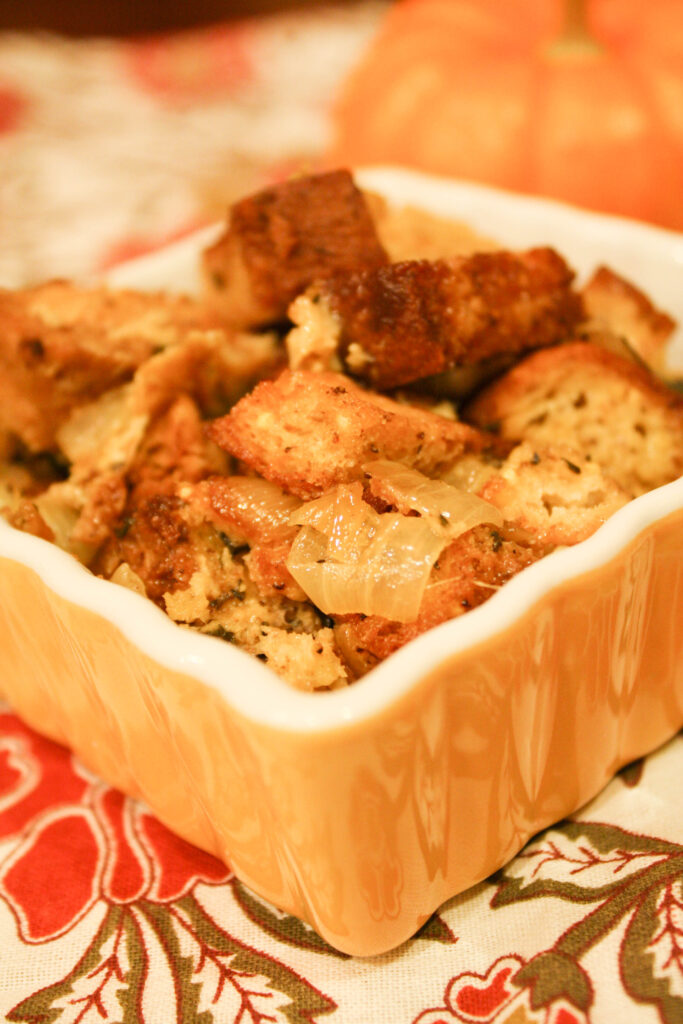 yellow and white square ramekin filled with savory stuffing on a fall themed cloth