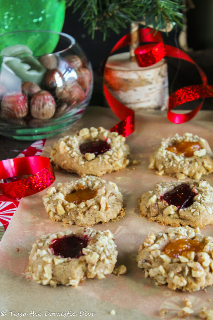 nut crusted thumbprint cookies filled with berry and apricot jam on an unbleached piece of parchment with festive Christmas ribbons and evergreen branches