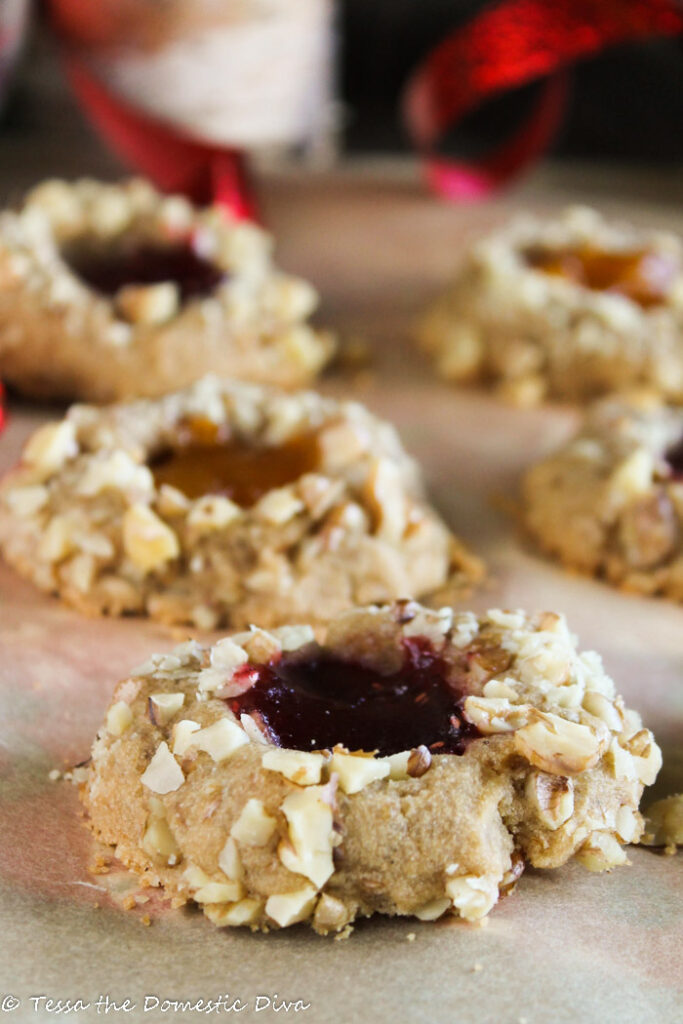 three jam filled thumbprint cookies with crushed walnuts on an unbleached parchment paper