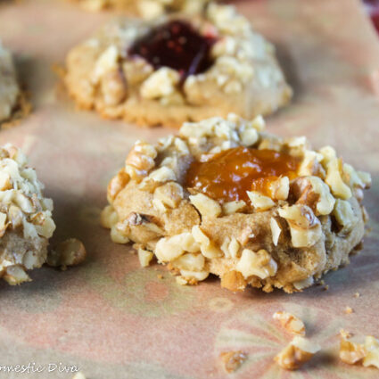 close up us a walnut coated thumbprint cookie with orange apricot jam filling on top of a holiday cloth