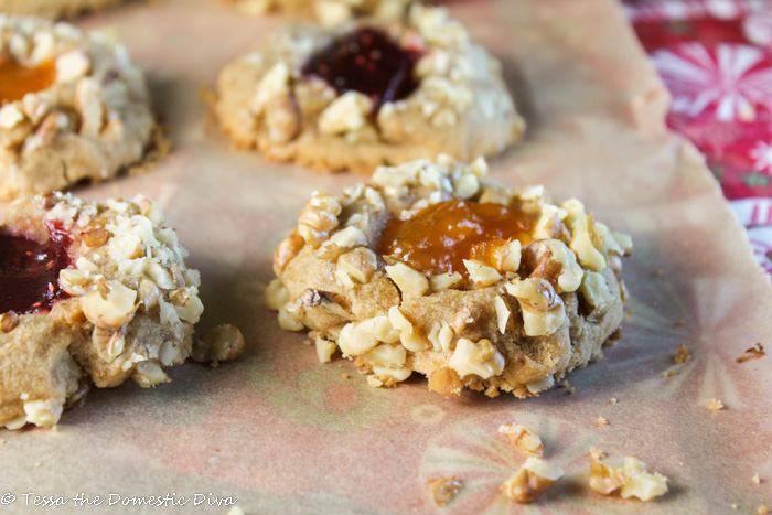 close up us a walnut coated thumbprint cookie with orange apricot jam filling on top of a holiday cloth