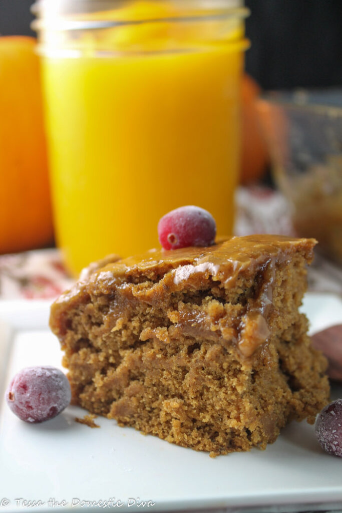 a square of moist pumpkin cake topped with a shiny caramel glaze and a fresh cranberry