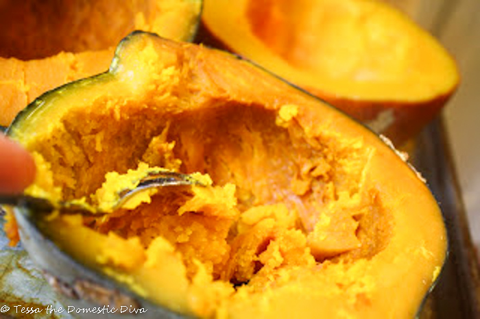 a halved cooked pumpkin with cooked flesh being scooped out with a metal spoon