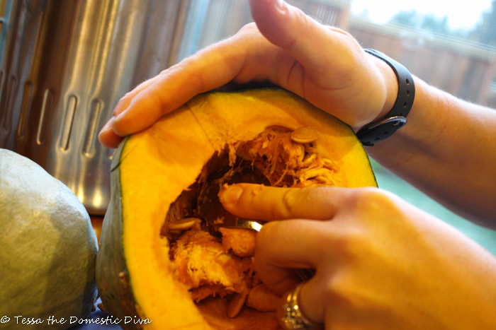 a halved kabocha squash with seeds being scraped out with metal spoon