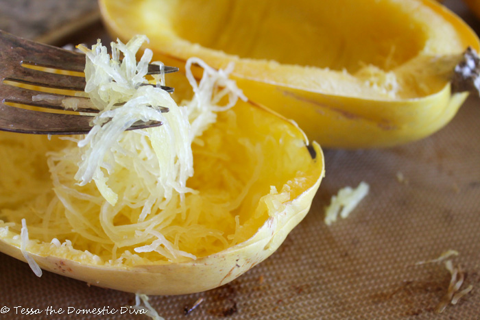 cooked spaghetti squash threads wrapped around a fork hovering above the cooked half