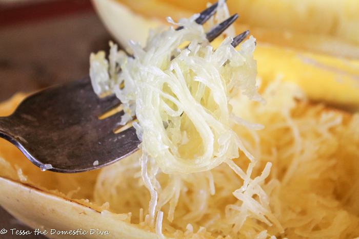 cooked threads of spaghetti squash around a fork hovering above a halved squash