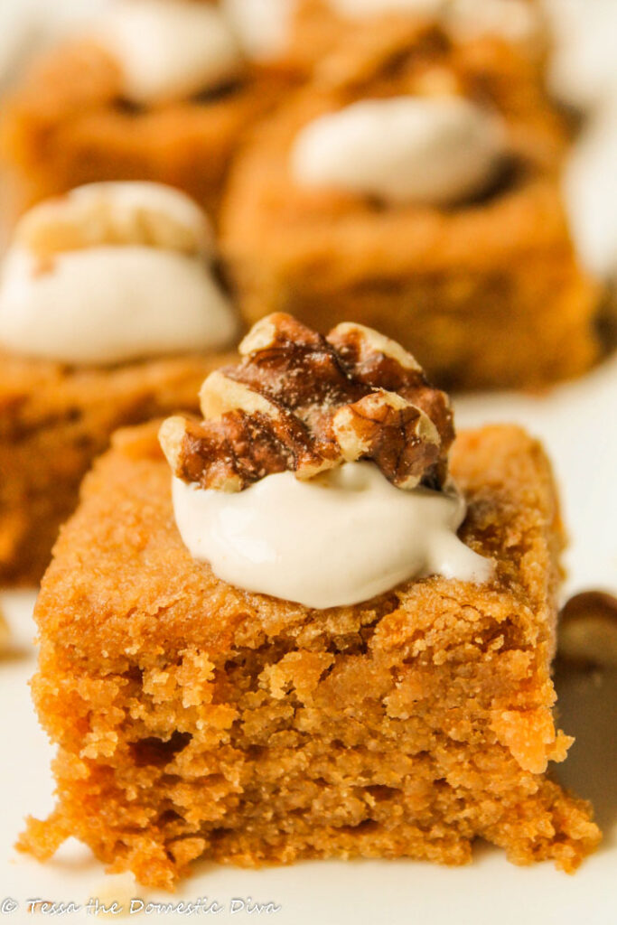 lose up of one square of tender paleo pumpkin cake topped with a dollop of brown butter cream cheese frosting and a walnut half