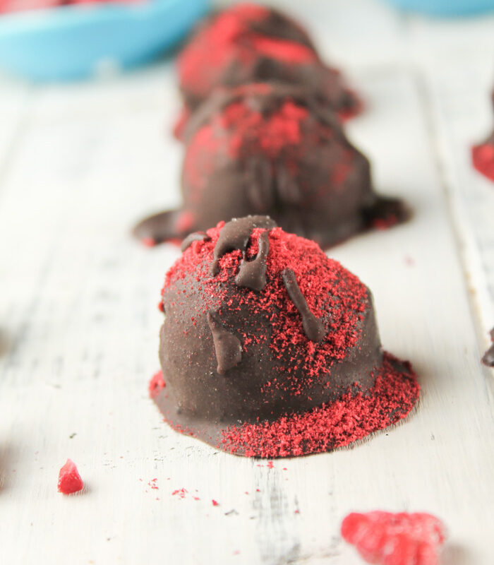 a row of red dusted homemade chocolate truffles on a white board with rapsberries