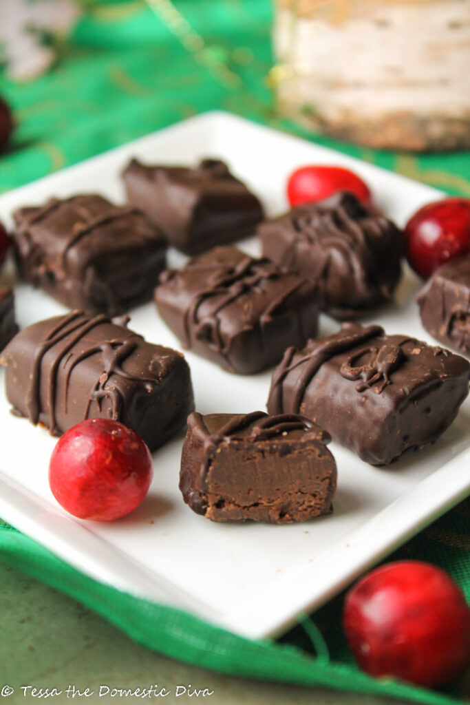 verical image of dipped chocolate mint truffles with one sliced for view of soft minty center on a white plate with fresh cranberries and a dark green tablecloth