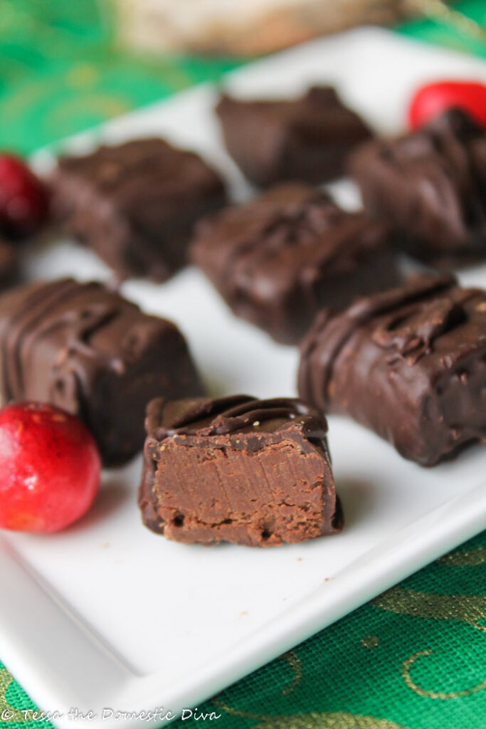 a halved chocolate dipped truffles with a creamy interior with a fresh cranberry on a white plate atop a Christmas green cloth