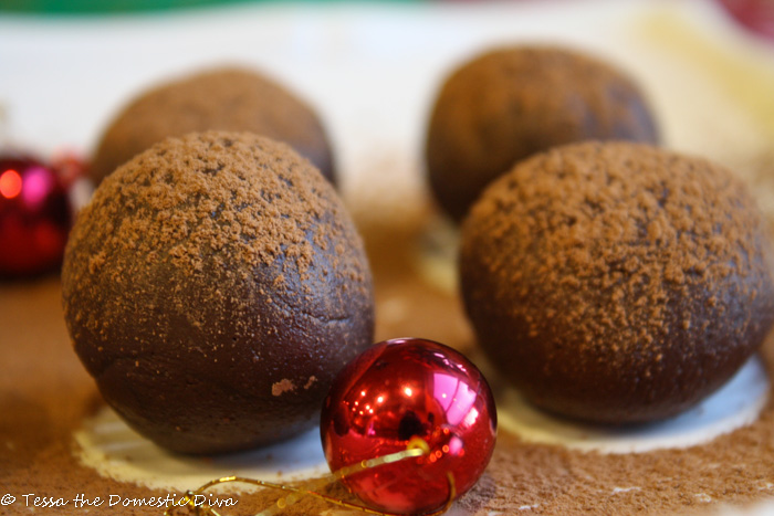 rolled chocolate truffles dusted with cocoa powder atop a white plate with a red ornament