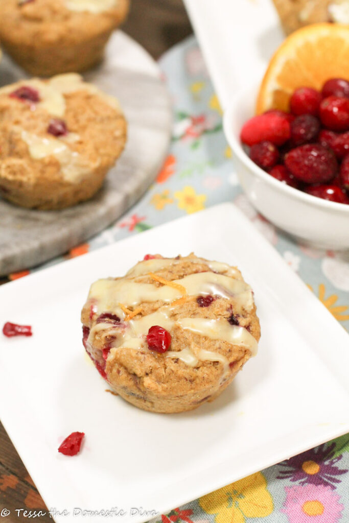 cranberry studded muffins with orange zest and a creamy glaze on a white plate