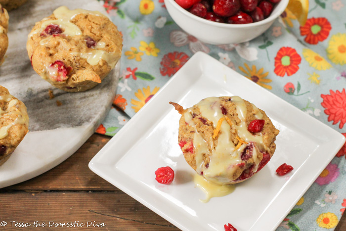 a white square plate with a cranberry studded muffin topped with a drizzle of orange glaze and zest