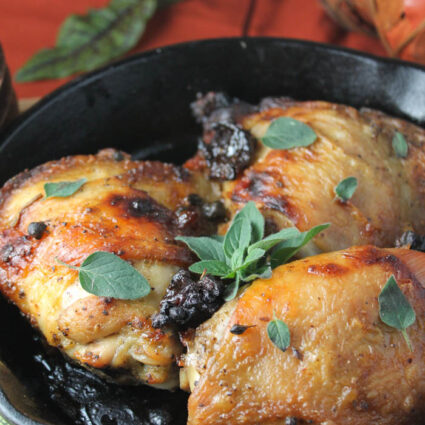 a black cast iron skillet filled with roasted chicken thighs with crispy skin and oregano, prunes. parsley