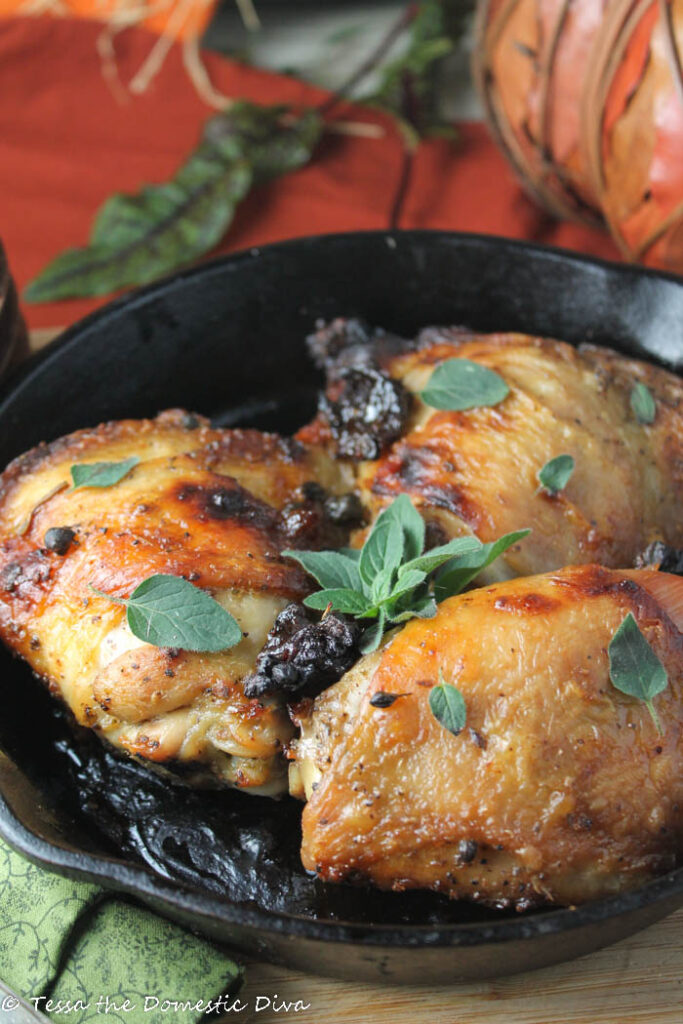 a black cast iron skillet filled with roasted chicken thighs with crispy skin and oregano, prunes. parsley