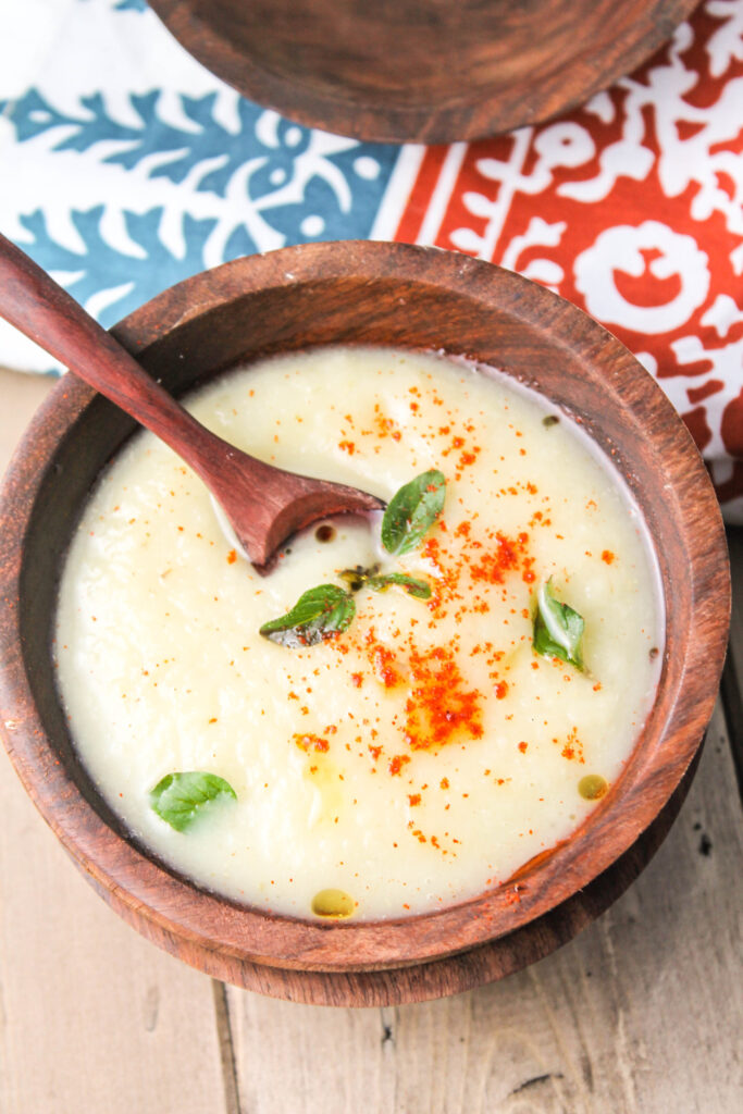 birds eye view of a dark wood bowl filled with a creamy white root vegetable soup with fresh oregano